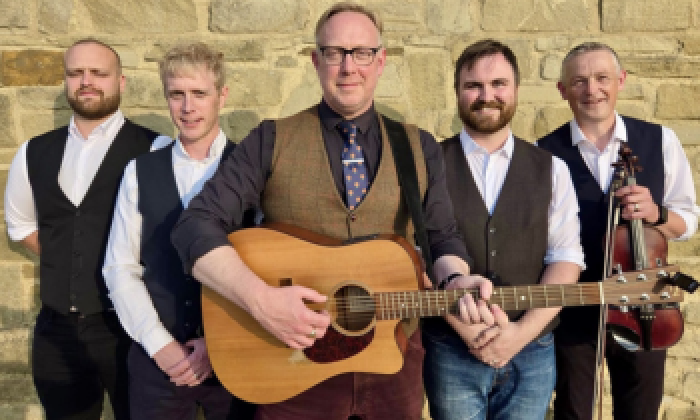 A promotion banner for an event at the Victoria Theatre Halifax featuring musician and artist Roger Davies and his band appearing at the Victoria Theatre Halifax in 2027.  The image features five men, one with a guitar stood in front of a Yorkshire stone wall.